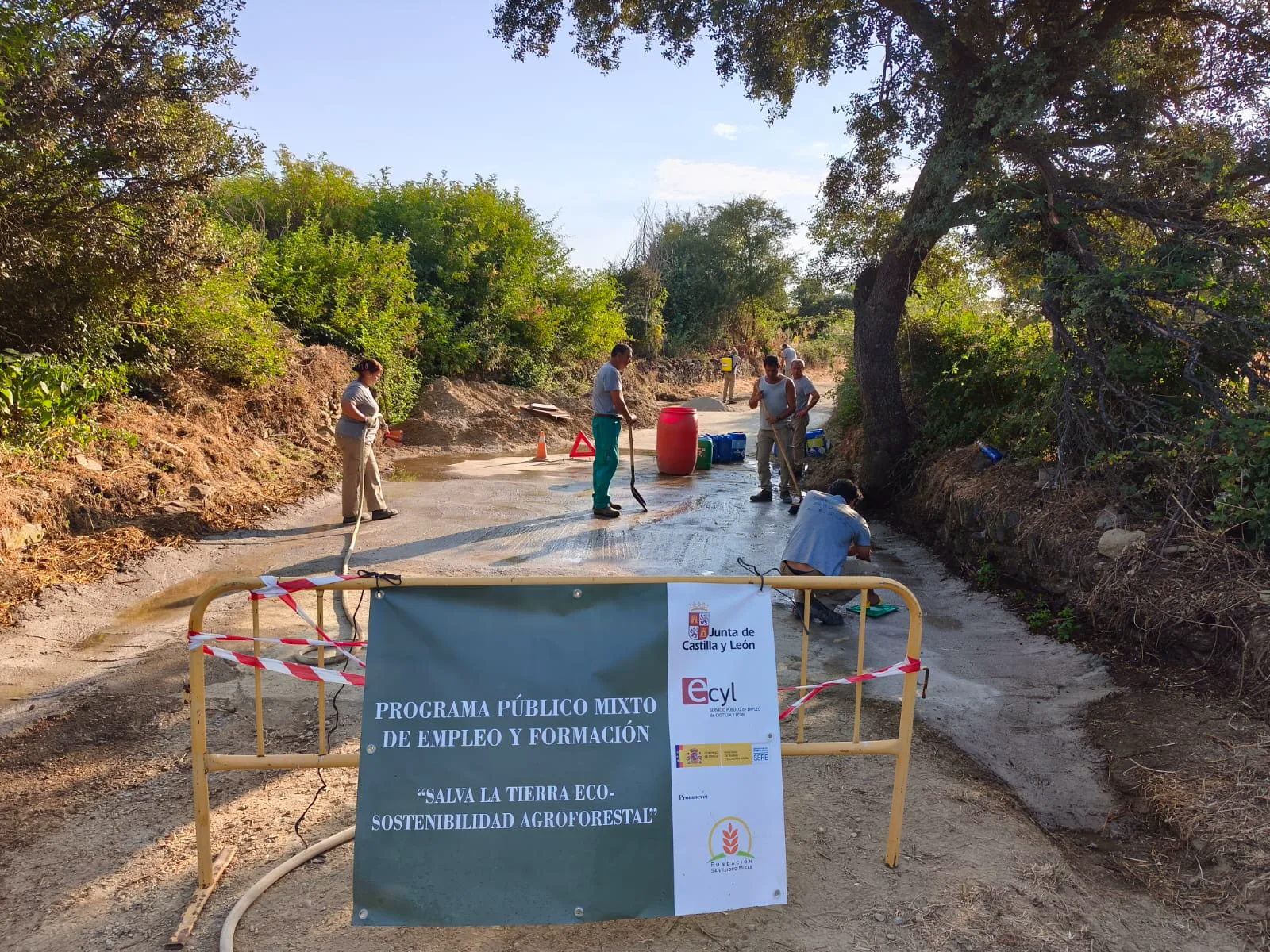 Participantes trabajando en el Camino de Prado Morán junto al cartel institucional del programa